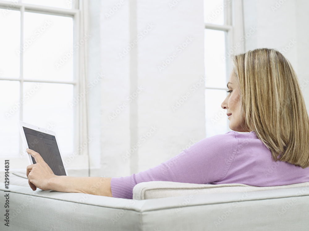 Side view of a middle aged woman using laptop on sofa at home Side view of a middle aged woman using laptop on sofa at home