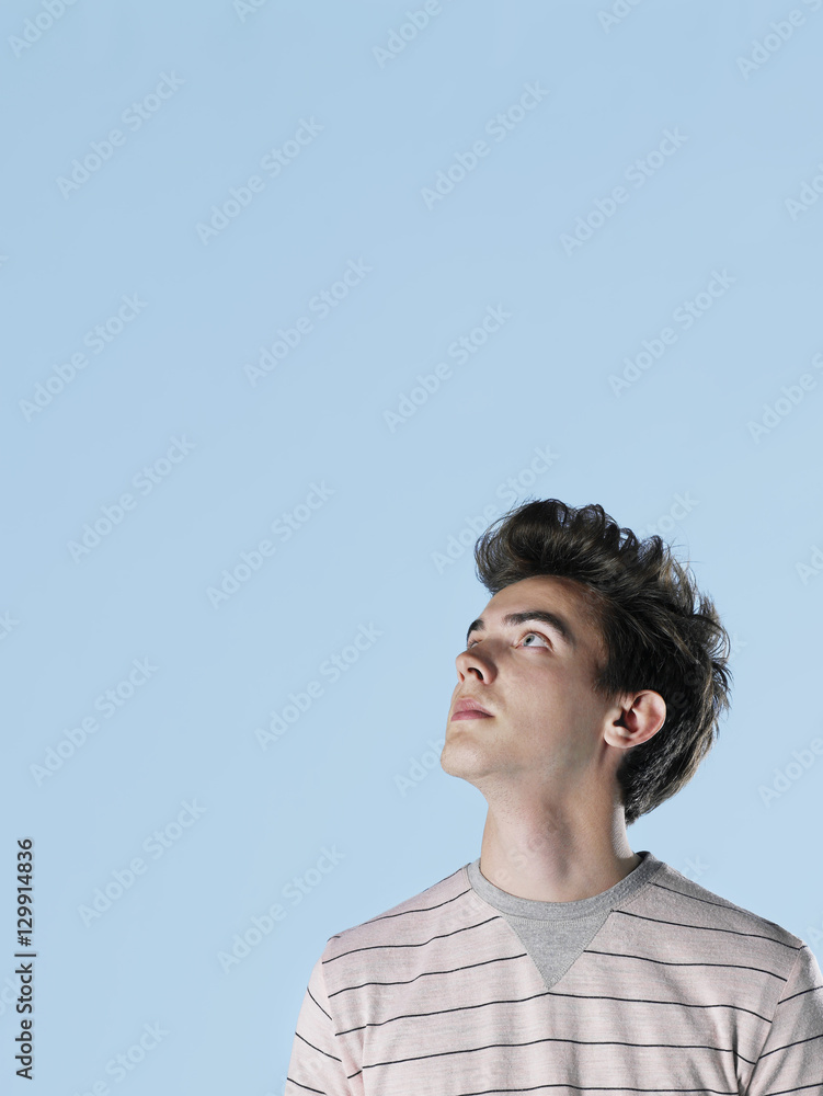 Young man looking up at copyspace on blue background Young man looking up at copyspace on blue background
