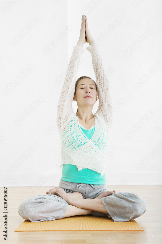 Full length of woman sitting cross legged with joined hands over head at gym Full length of woman sitting cross legged with joined hands over head at gym