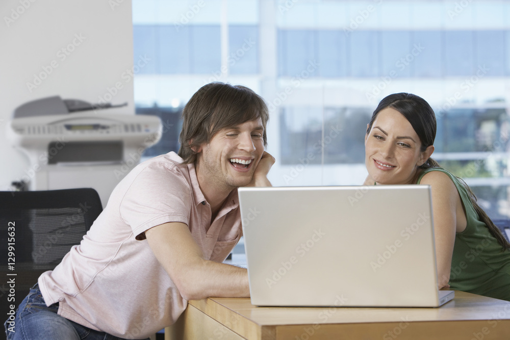 Cheerful business colleagues using laptop at desk in office Cheerful business colleagues using laptop at desk in office