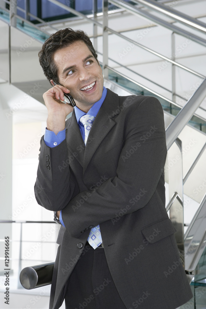 Happy businessman looking away while using mobile phone by railing in office Happy businessman looking away while using mobile phone by railing in office
