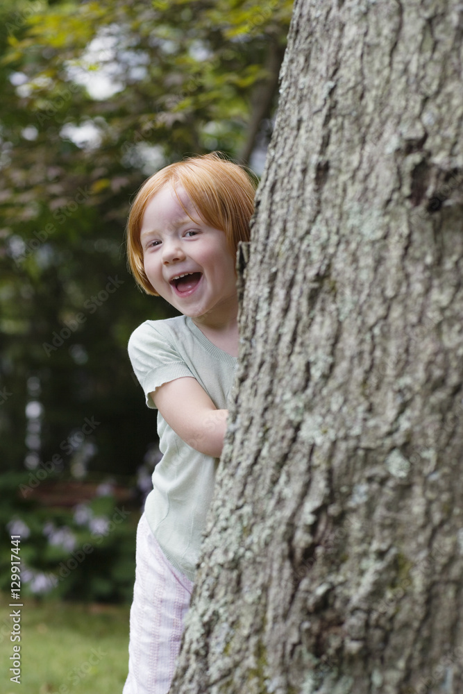 Portrait of a cheerful little girl peeking from behind tree Portrait of a cheerful little girl peeking from behind tree
