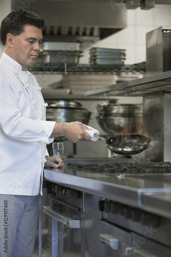 Side view of a male chef cooking food using frying pan in kitchen