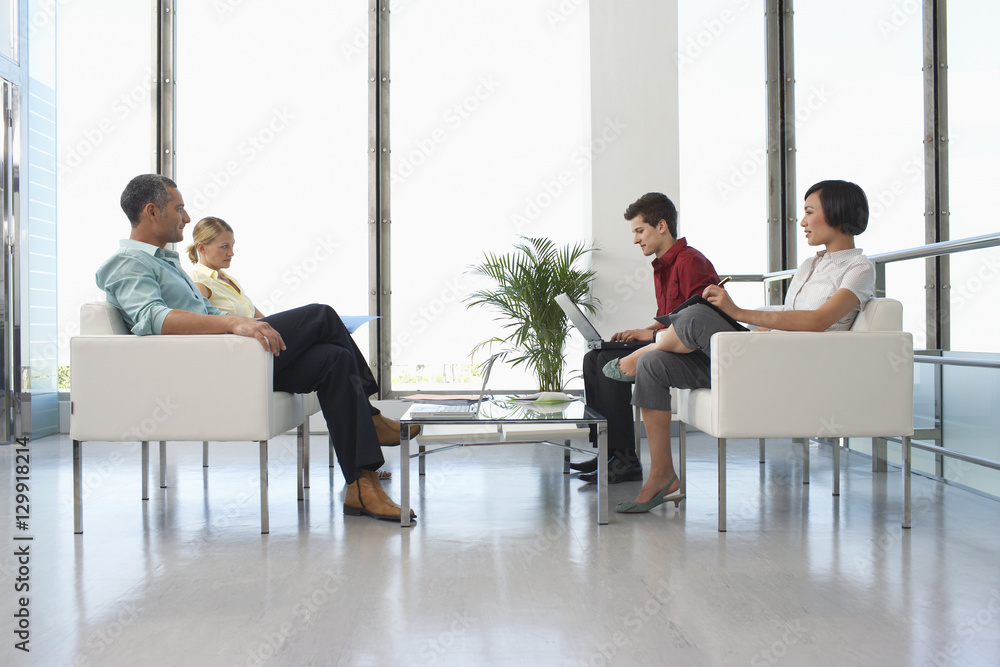 Full length side view of four business people sitting in modern waiting room at office Full length side view of four business people sitting in modern waiting room at office