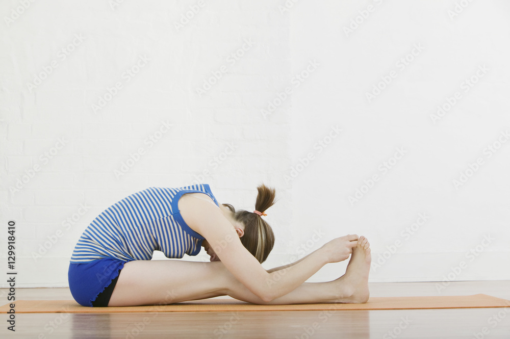 Profile shot of woman doing Seated Forward Bend in gym Profile shot of woman doing Seated Forward Bend in gym