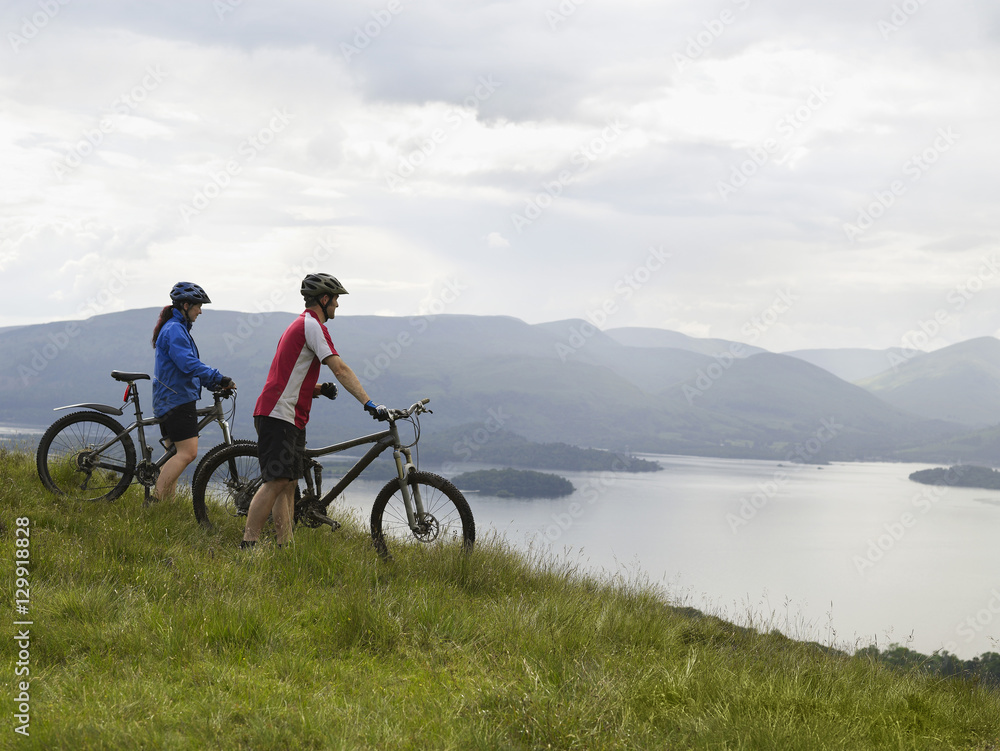 Fototapeta premium Side view of a couple with bicycles near the peaceful lake