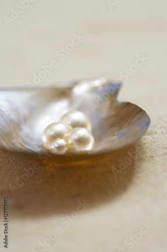 Four pearls in open oyster shell on beach close up