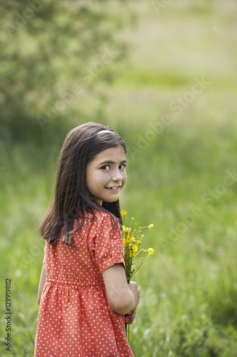 Portrait of happy young girl holding flowers in field