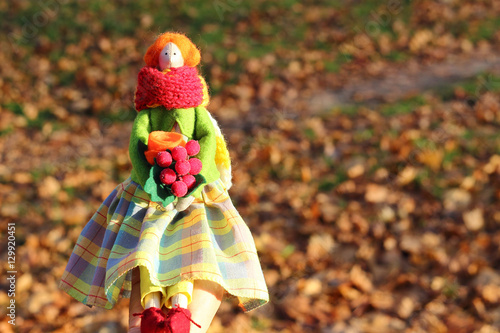 Handmade doll girl tilda in a plaid skirt  a red scarf and a bouquet on autumn background. Interior fairy dolls
