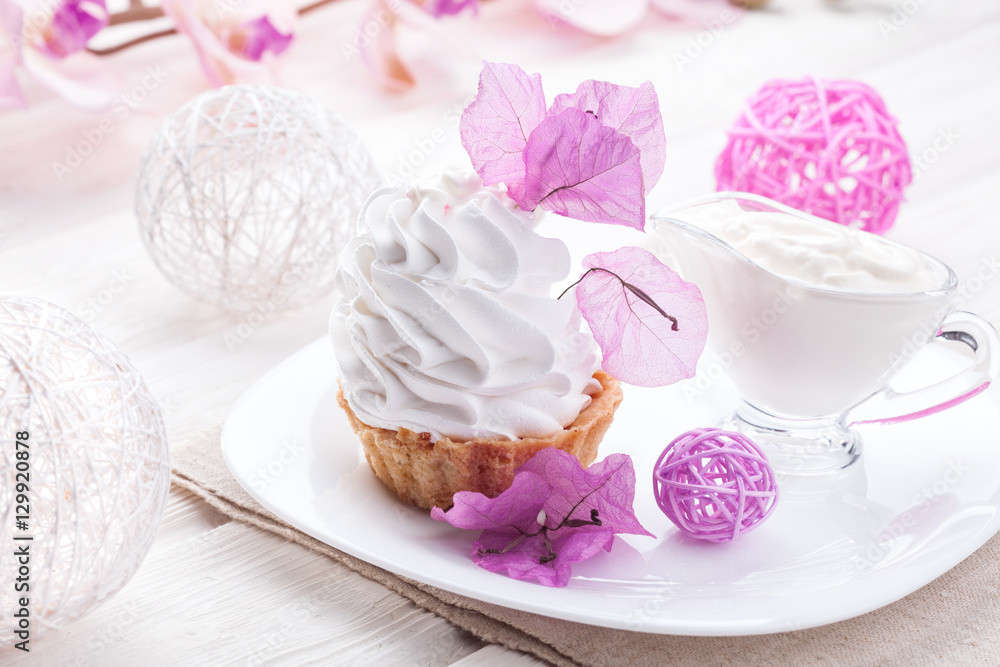 White cake with cream protein with the decor of pink flowers on a wooden table