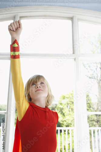 Serious young boy in superhero costume with raised fist looking up
