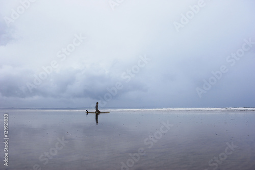 Young man with surfboard sitting on beach