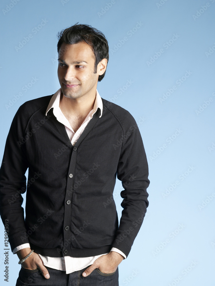 Fototapeta premium Portrait of handsome young man with hands in pockets standing isolated on blue background