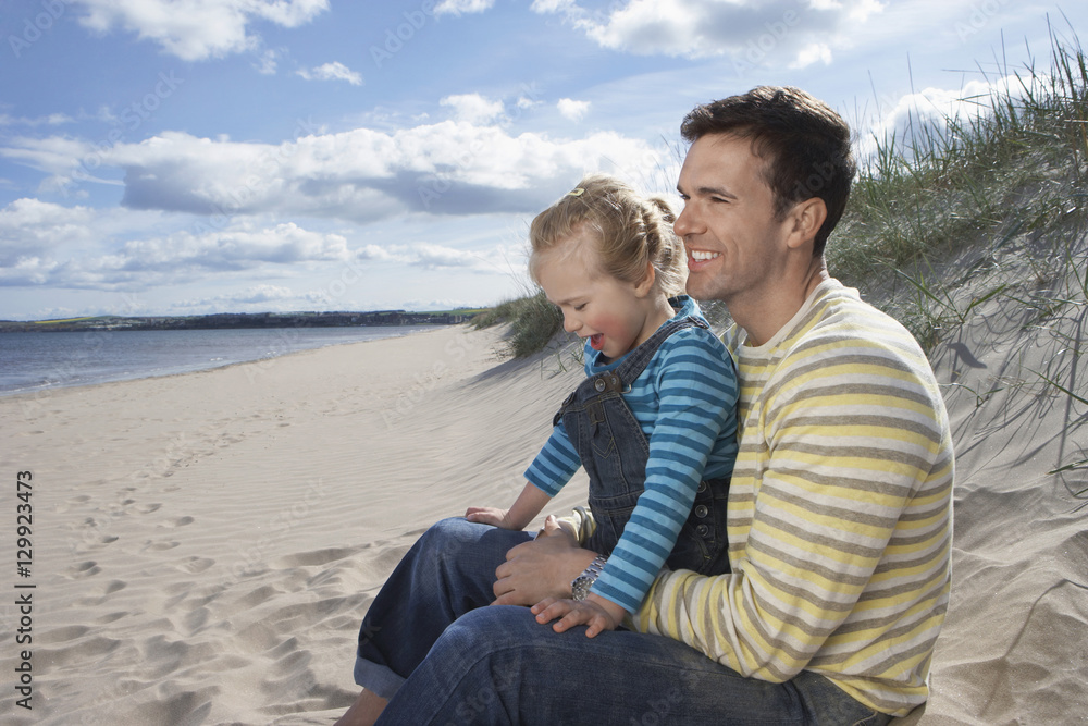 Happy father and daughter sitting on sandy beach Happy father and daughter sitting on sandy beach
