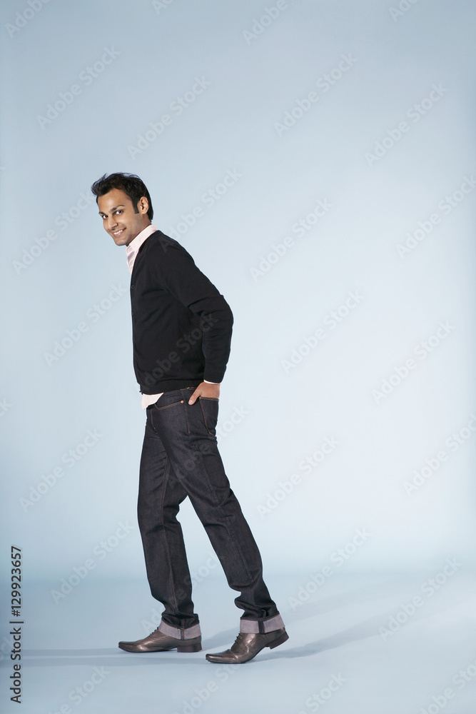 Portrait of smiling young man walking with hand in back pocket isolated on blue background Portrait of smiling young man walking with hand in back pocket isolated on blue background