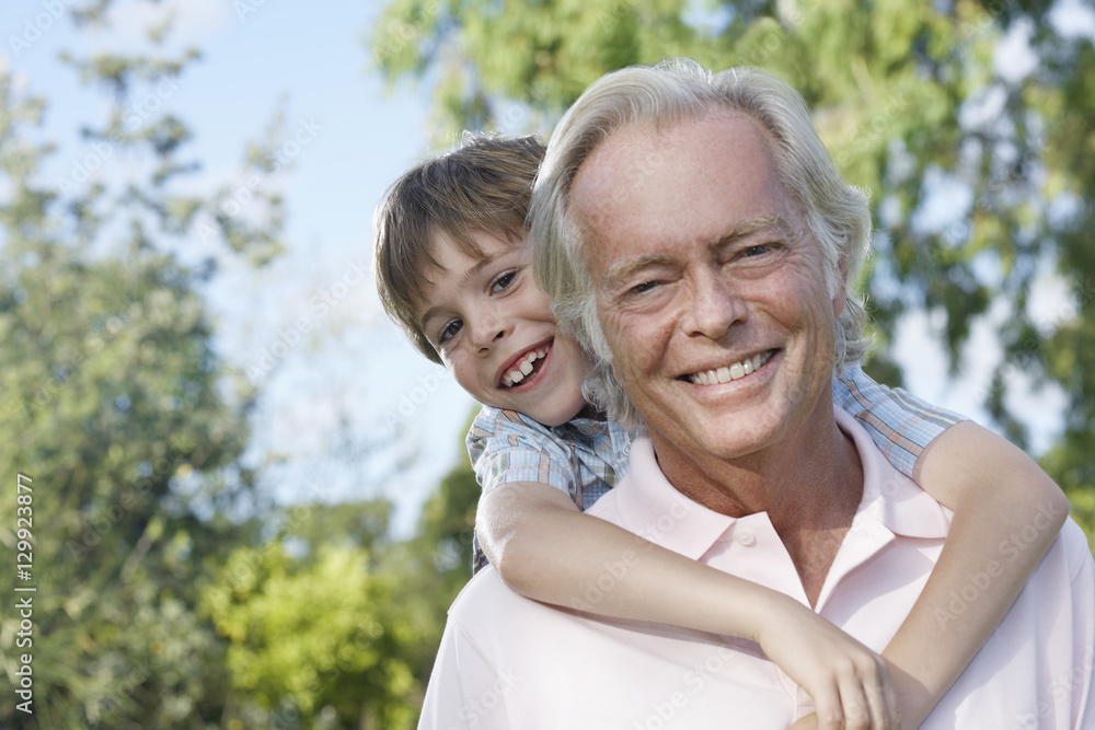 Closeup portrait of a smiling grandfather with grandson riding piggyback outdoors Closeup portrait of a smiling grandfather with grandson riding piggyback outdoors