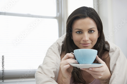 Portrait of beautiful young woman wrapped in duvet drinking tea
