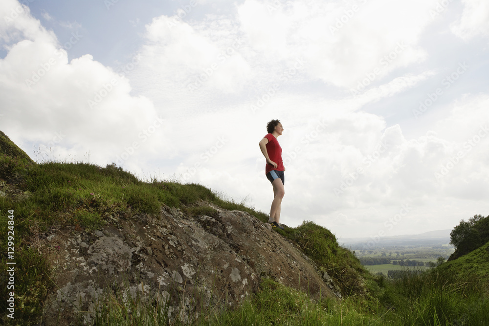 Full length side view of a female hiker standing on hill against clouds Full length side view of a female hiker standing on hill against clouds