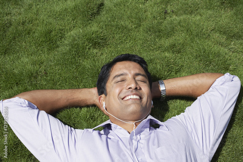 Closeup of happy young businessman listening music while lying on grass