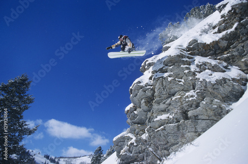 Low angle view of a person on snowboard jumping midair over cliff photo