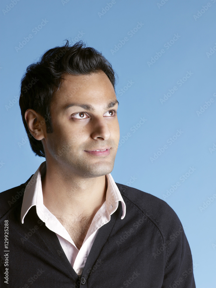 Closeup of handsome young man looking up and smiling on blue background Closeup of handsome young man looking up and smiling on blue background