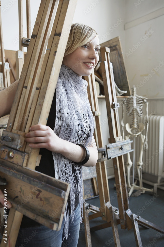 Young female art student carrying easel into studio
