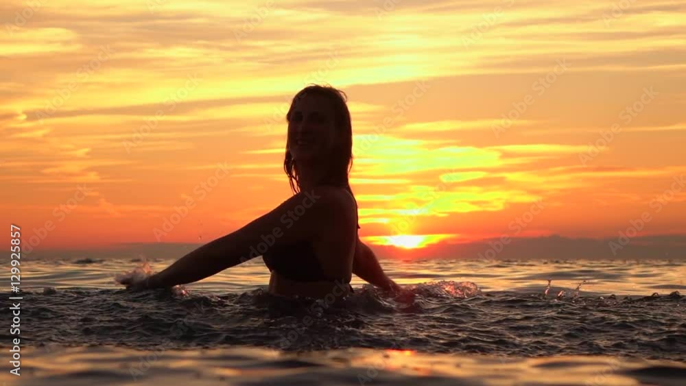 SLOW MOTION: Attractive young girl playing with water in ocean at golden sunset SLOW MOTION: Attractive young girl playing with water in ocean at golden sunset