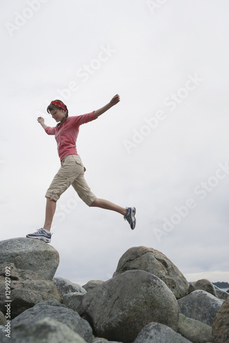 Full length low angle view of a young woman jumping with arms raised over rocks