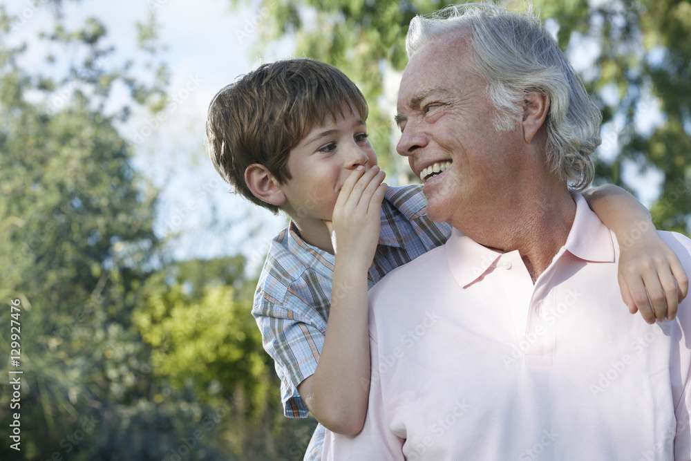 Closeup of a young boy whispering in grandfather's ear outdoors Closeup of a young boy whispering in grandfather's ear outdoors