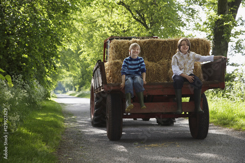 Full length portrait of two young boys sitting on back of trailer on country lane © moodboard