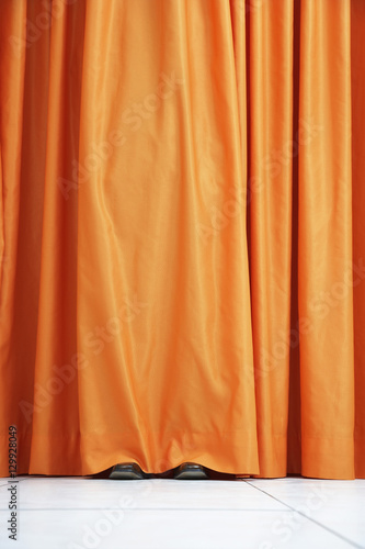 View of shoes seen hiding behind orange curtain