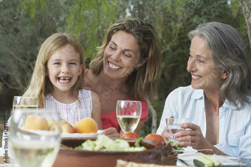 Portrait of grandmother  mother and cheerful daughter sitting at table in garden