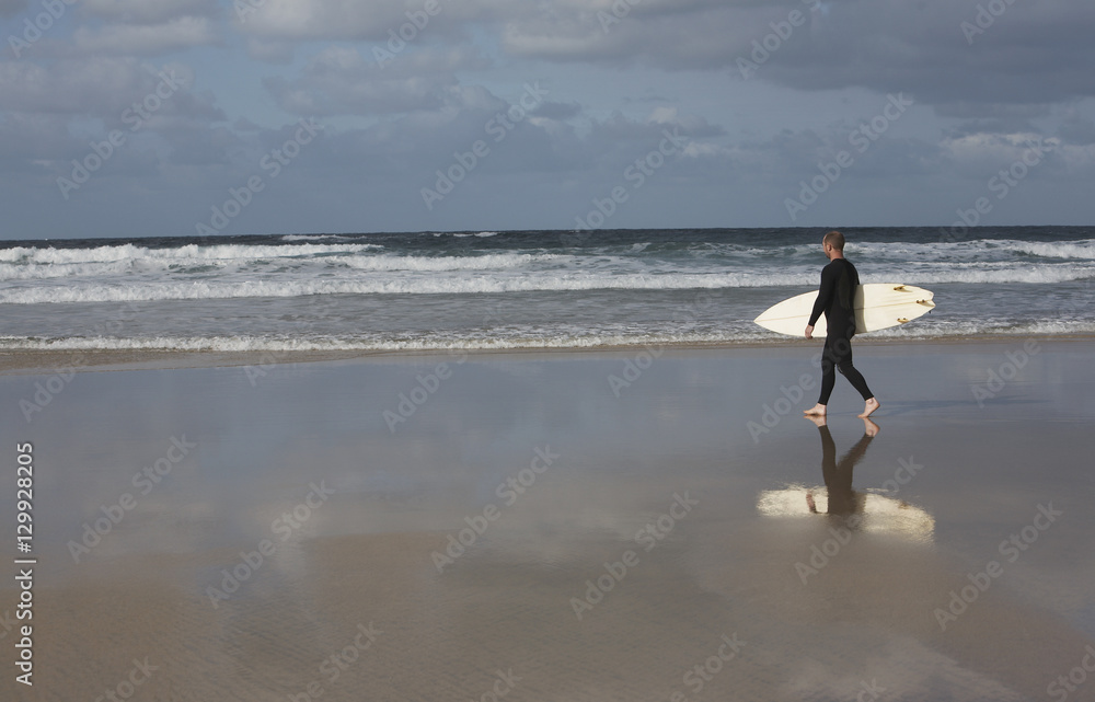 Side view of man with surfboard walking towards ocean Side view of man with surfboard walking towards ocean