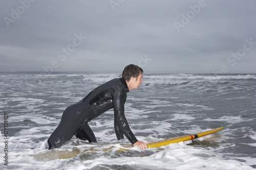Profile shot of young man in wetsuit surfing at beach