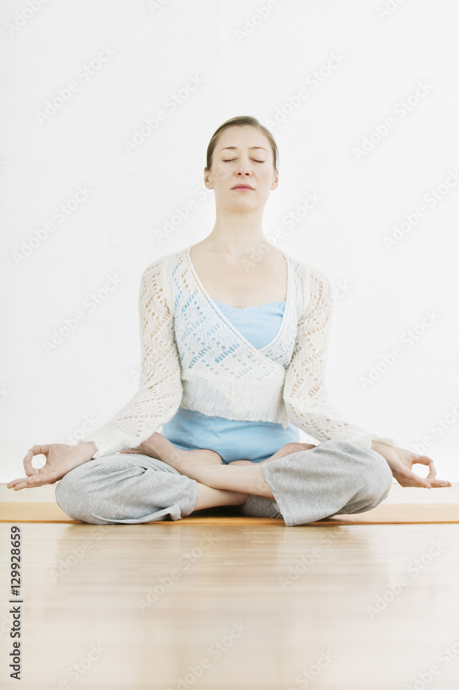 Full length of fit woman meditating in lotus position at gym
