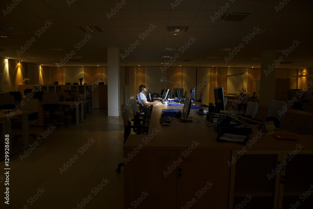 Side view of a young woman working on computer in dark office