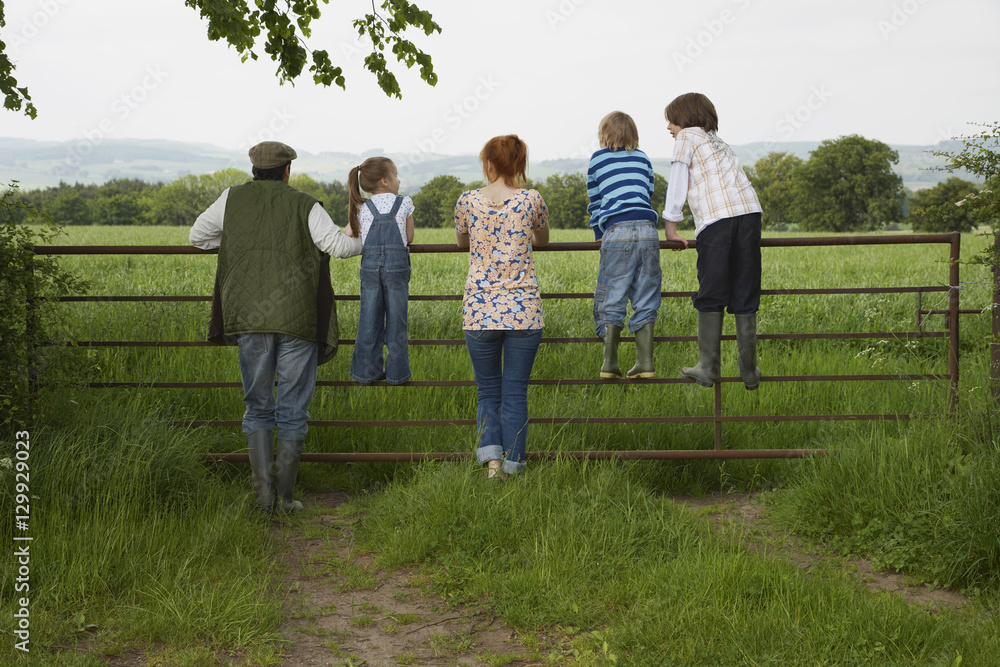 Full length rear view of couple with three children looking at lush landscape by fence Full length rear view of couple with three children looking at lush landscape by fence