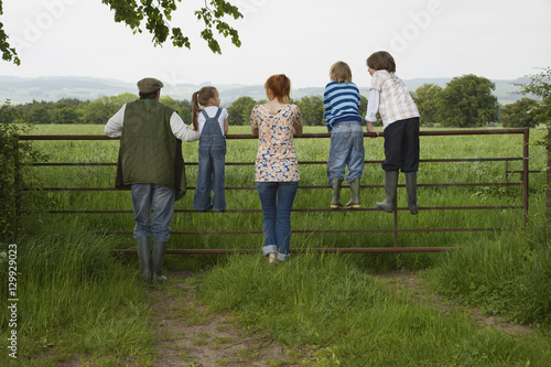 Full length rear view of couple with three children looking at lush landscape by fence