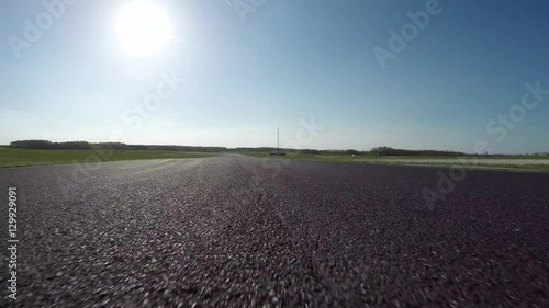 FPV LOW ANGLE: Racecar driving fast competing on racetrack on sunny day photo