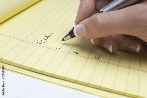 Closeup of female's hand writing list of goals on notepad