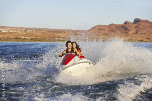 Happy young Caucasian couple riding water scooter on lake © moodboard