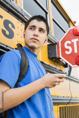 High school boy listening music on mp3 player by school bus photo