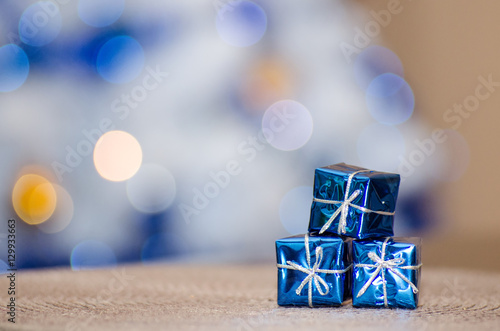 Trzy prezenty w ozdobnych niebieskich opakowaniach na tle rozmytych świateł z choinki