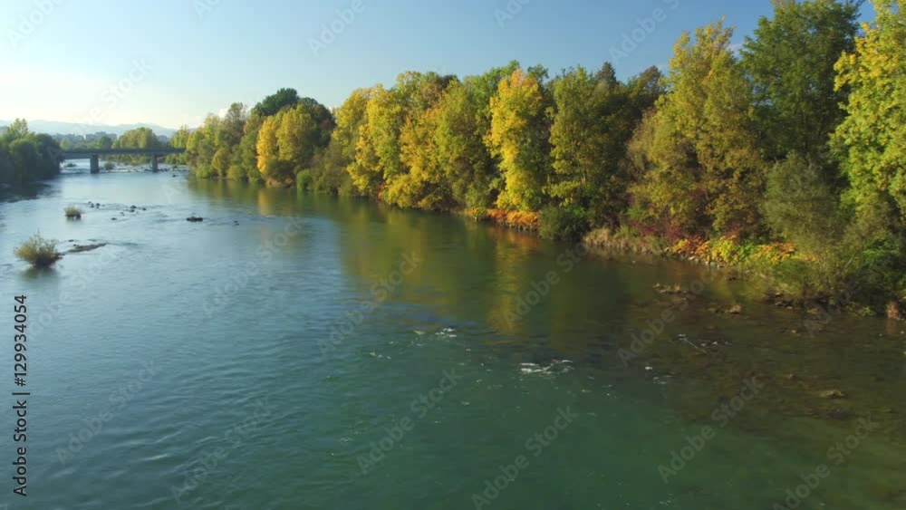 AERIAL: Beautiful wide river with green lush riverbank and big town in distance