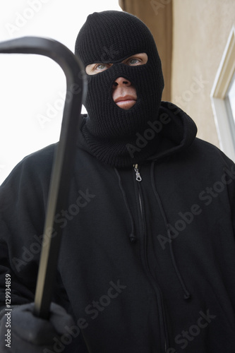 Burglar wearing balaclava and holding crowbar outside house