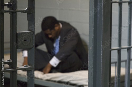 A depressed businessman sitting on bed in prison cell © moodboard