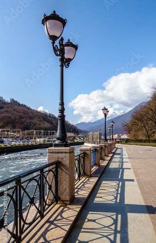 Vanishing row of street lantern pillars on the river enbankment in Rosa Khoutor mountain resort, Sochi, Russia photo