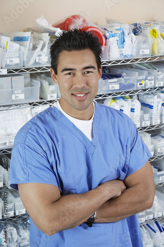 Portrait of male nurse standing by shelves with medical supply