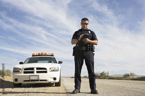 Billede på lærred Full length of a police officer writing on clipboard while standing in front of