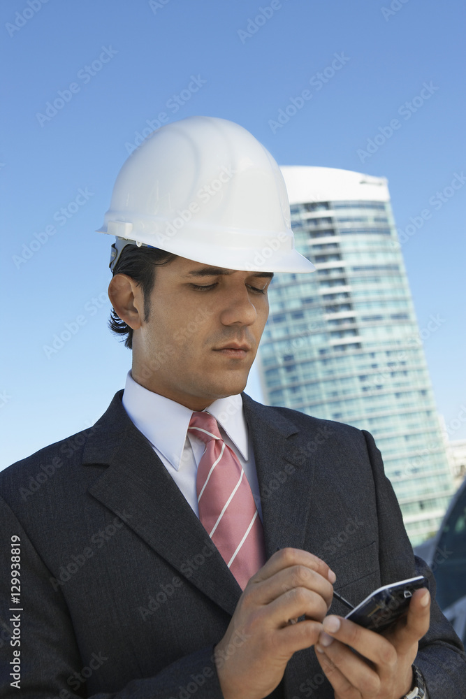 Businessman in hardhat using PDA outdoors